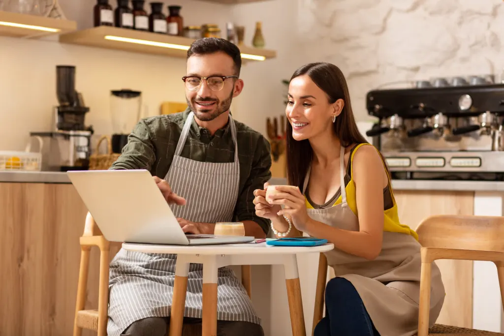 Los dueños de una cafetería revisan su web juntos en el portátil, en su propio local